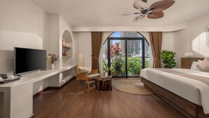 A modern hotel room with a flat-screen TV, a wooden coffee table, a comfortable chair, a large bed, and a view of the city through floor-to-ceiling windows. - Saha Casa Boutique Hotel Da Nang (Da Nang)