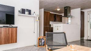 Een moderne keuken met witte bakstenen muren, houten kasten en een inbouwfornuis. Er is een eethoek met een houten tafel en stoelen, en een aan de muur bevestigde televisie.