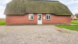 Een rieten cottage met een grindpad en een grasveld op de achtergrond.