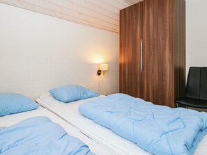 Une chambre avec deux lits, une armoire en bois et une lampe fixée au mur.