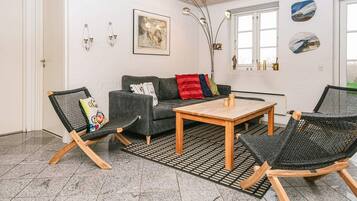 Una sala de estar moderna con un sofá gris, dos sillas de mimbre negro, una mesa de centro de madera y una alfombra estampada.