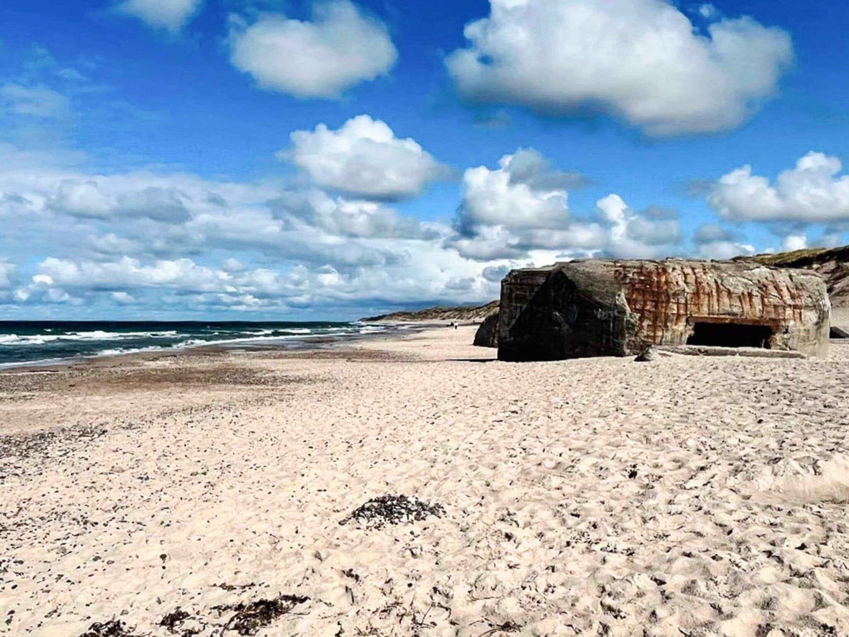 Una playa con una gran formación rocosa y el océano al fondo.