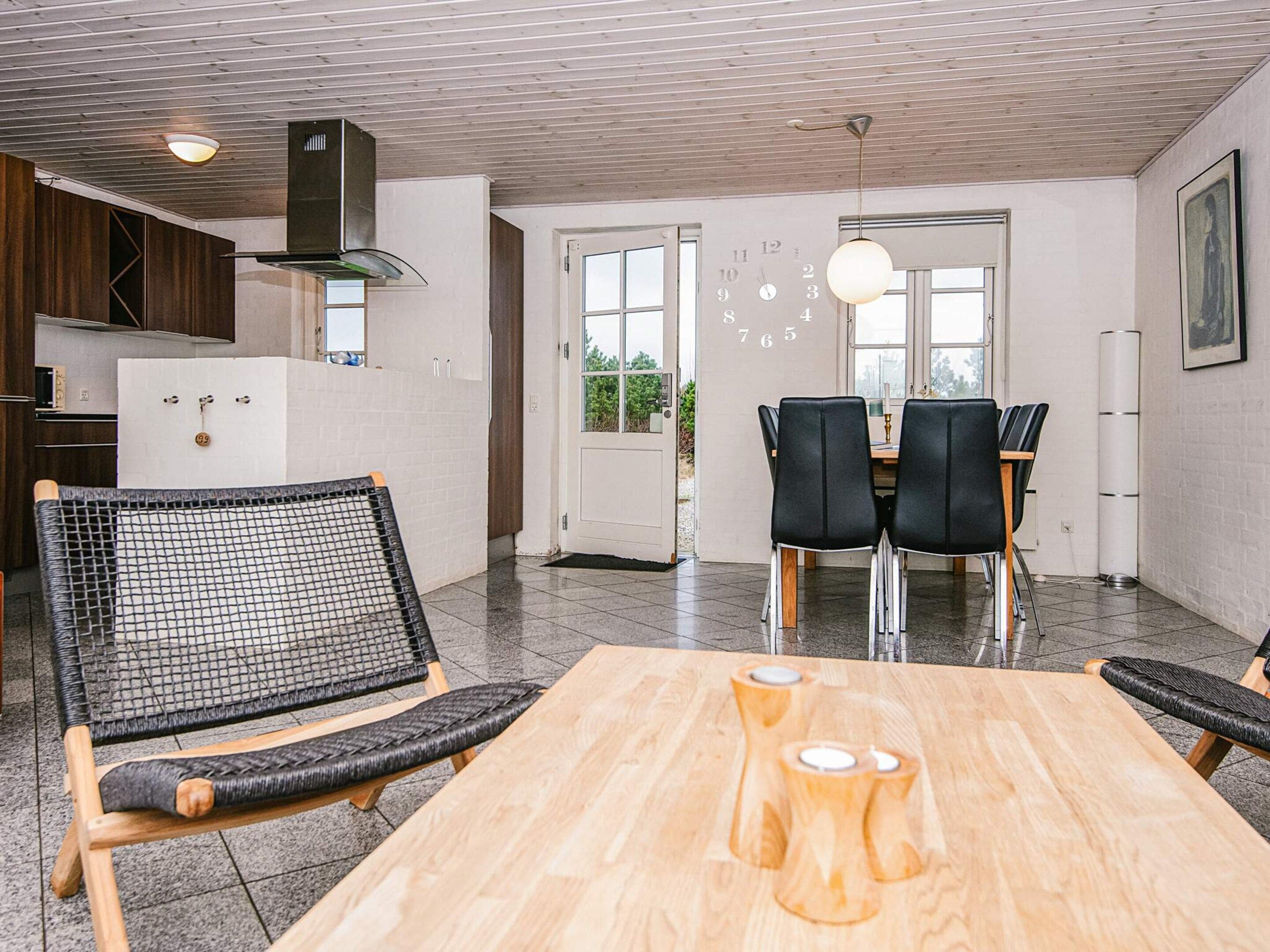 Una cocina moderna con estufa integrada, un comedor con mesa de madera y sillas negras, y un ventanal con vistas a zonas verdes.