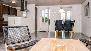 Una cocina moderna con estufa integrada, un comedor con mesa de madera y sillas negras, y un ventanal con vistas a zonas verdes.