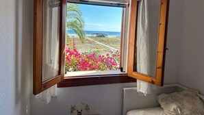 Une chambre avec une baie vitrée donnant sur la plage, un lit et une petite table sur laquelle est posé un vase.
