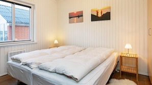 A double bed with white bedding, a window with blinds, two wall-mounted lamps, and two framed pictures. - 5 Person Holiday Home on a Holiday Park in Lemvig (Lemvig)