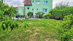 A two-story house with a green facade and a red-tiled roof, surrounded by a well-maintained garden with various plants and a bench. - Wonderful private villa for 5 guests with WIFI, TV and terrace (Chlumec Nad Cidlinou)
