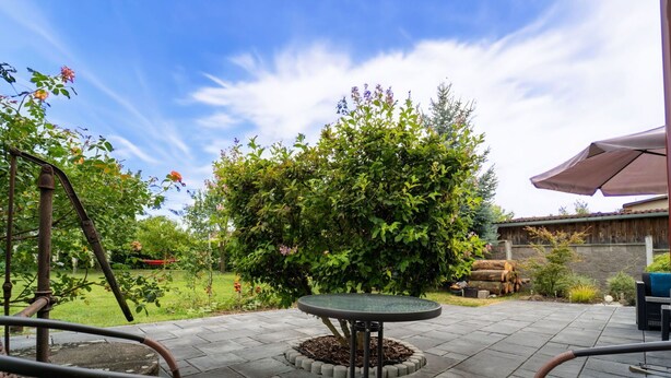 An outdoor patio with a round table and two wicker chairs, surrounded by a garden with various plants and a wooden fence in the background. - Wonderful private villa for 5 guests with WIFI, TV and terrace (Chlumec Nad Cidlinou)