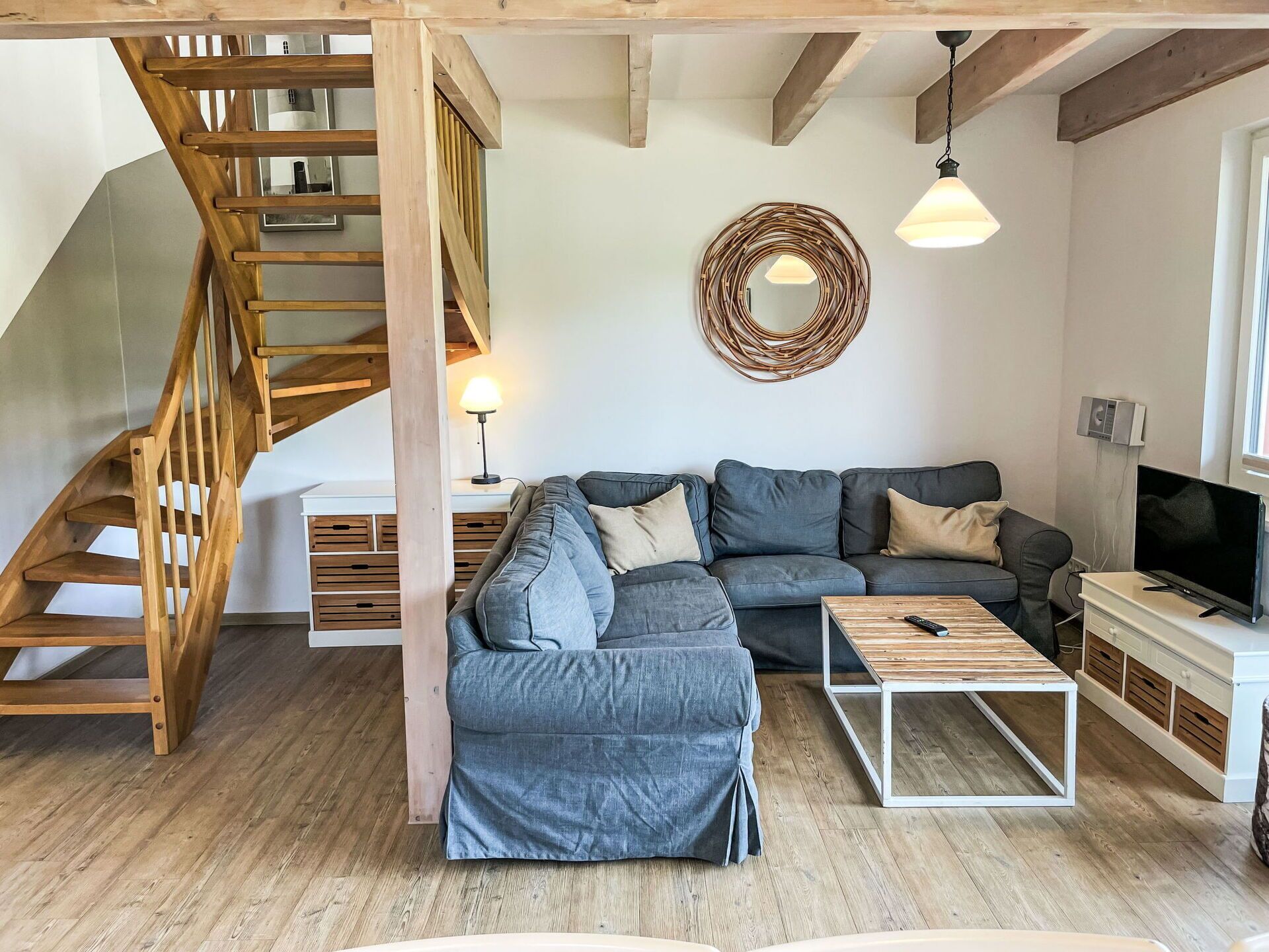 Ein modernes Wohnzimmer mit einer Holztreppe, einem grauen Ecksofa, einem Couchtisch und einem Fernseher.