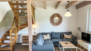 Una sala de estar moderna con una escalera de madera, un sofá seccional gris, una mesa de centro y un televisor.