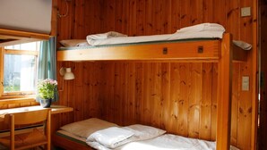Ein Schlafraum mit Etagenbetten, Holzwänden, einem Schreibtisch und einem Stuhl.