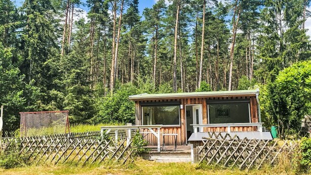 Une petite cabane avec une façade en bois, une véranda et un espace clôturé.