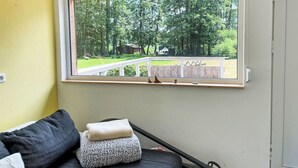 Une pièce avec une fenêtre donnant sur un paysage verdoyant, un lit avec des oreillers et un mur blanc.