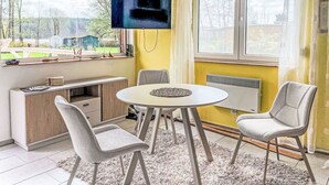 Une pièce comprenant une table à manger, deux chaises, un téléviseur fixé au mur, une fenêtre avec des rideaux et un radiateur.