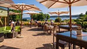 Une terrasse extérieure aménagée avec des meubles en osier, de grands parasols et une vue sur un lac.