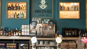 Un espace bar avec des étagères remplies de bouteilles d’alcool, un appareil à café et une enseigne indiquant « Ankerplatz ».