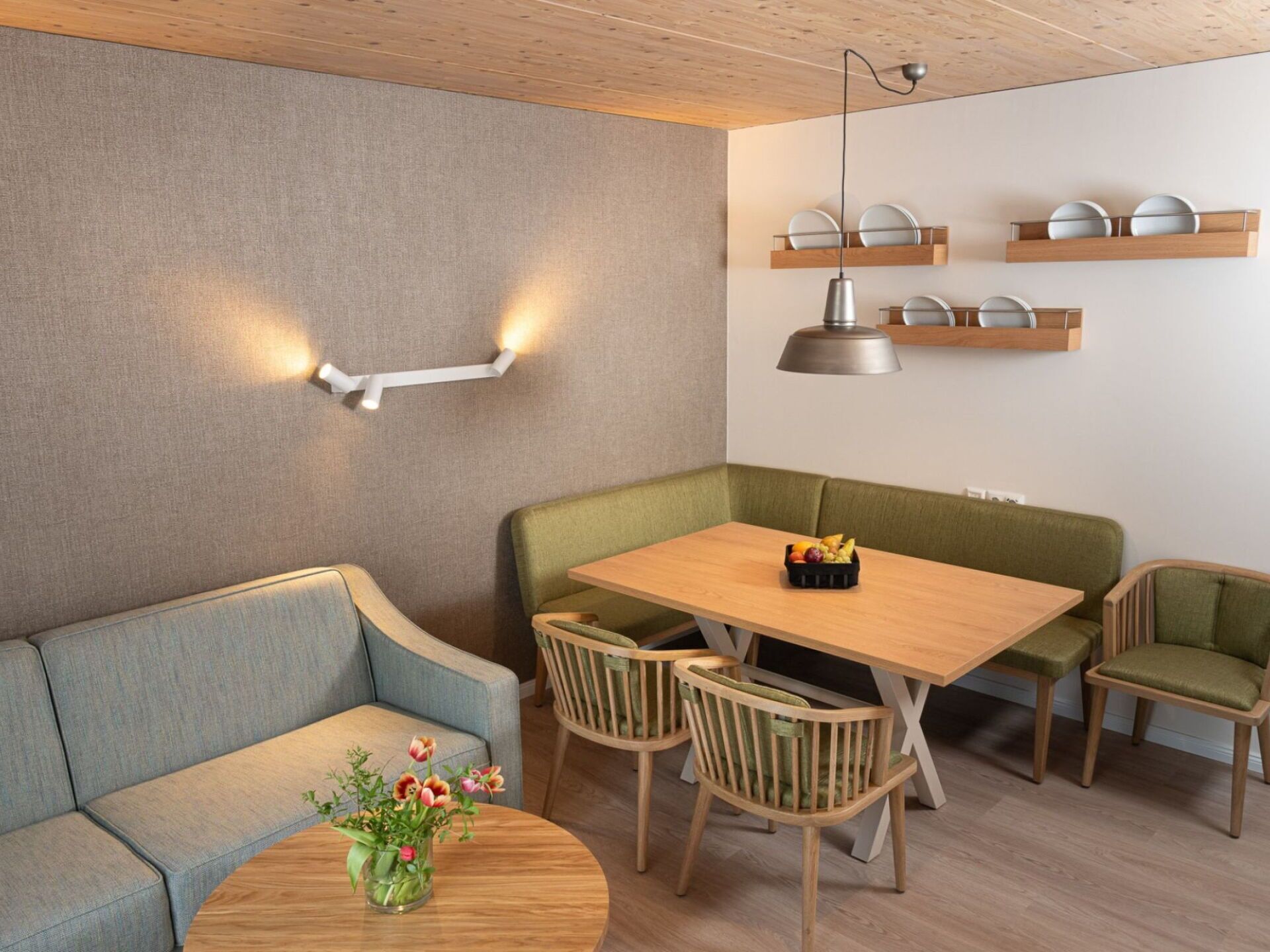 Een moderne eetruimte met een houten tafel, groene beklede stoelen en een bank.