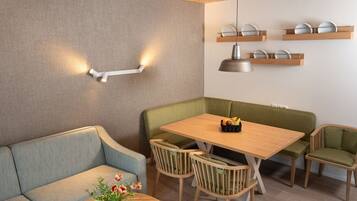 Een moderne eetruimte met een houten tafel, groene beklede stoelen en een bank.