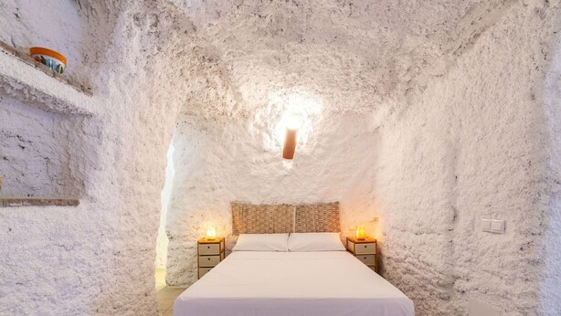 Un dormitorio con cama, dos mesitas de noche y una lámpara fijada a la pared.