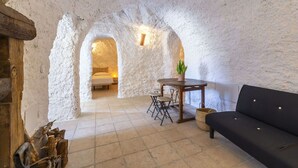 Una habitación acogedora con una pared de piedra rústica, una mesa de madera con sillas, un sofá negro y una cama al fondo.