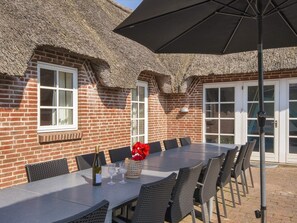A brick building with a thatched roof, a table with chairs, and an umbrella. - 4 Star Holiday Home in Ulfborg (Ulfborg)