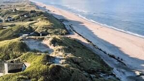 Paesaggio costiero con spiaggia, dune e alcuni edifici sparsi.