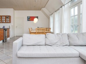 A modern living room with a sofa, dining table, and chairs. There is a kitchen area with cabinets and a refrigerator. - 4 Star Holiday Home in Ulfborg (Ulfborg)