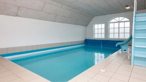 Una piscina interna con uno scivolo blu, pareti piastrellate e un soffitto inclinato.