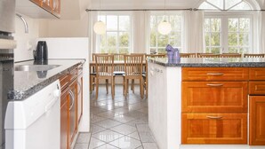 A kitchen with a granite countertop, wooden cabinets, a coffee maker, and a dining area with wooden chairs and a table. - 4 Star Holiday Home in Ulfborg (Ulfborg)