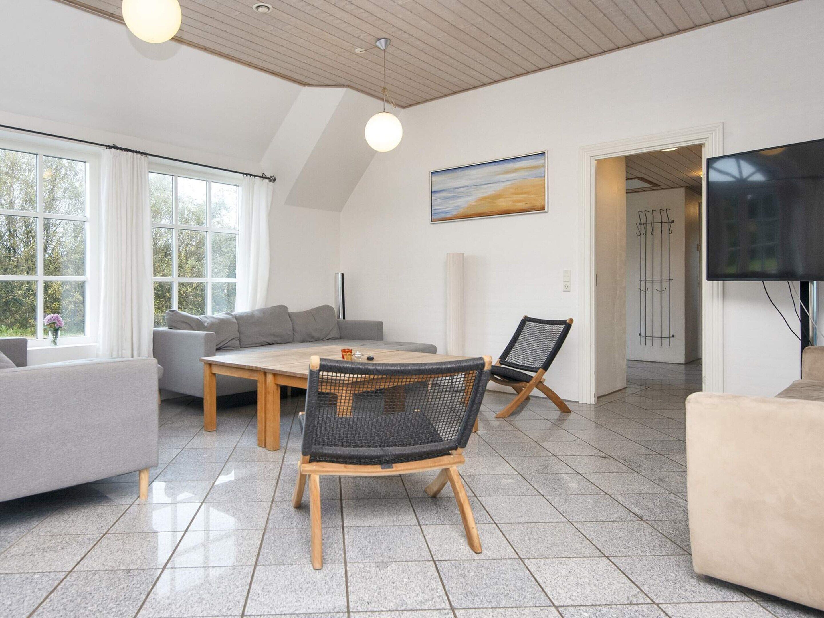 Uma sala de estar moderna com um sofá, uma mesa de jantar e cadeiras. Há um quadro na parede e uma TV fixada na parede.
