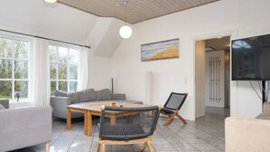 A modern living room with a sofa, a dining table, and chairs. There is a painting on the wall and a TV mounted on the wall. - 4 Star Holiday Home in Ulfborg (Ulfborg)