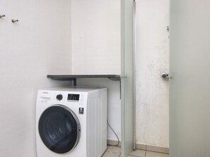 A compact, white washing machine in a small utility room with a door and a metal shelf above it. - 4 Star Holiday Home in Ulfborg (Ulfborg)