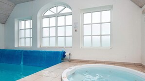 Una piscina interna con una vasca idromassaggio, due ampie finestre ad arco e un telo blu.