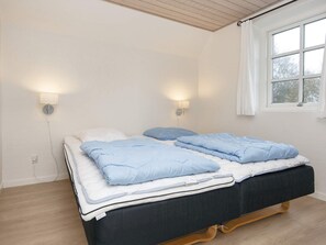 Una cama doble con cabecera oscura, dos lámparas de noche y una ventana con cortinas.
