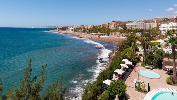 Un hôtel situé sur la côte, avec vue sur la plage, une piscine et plusieurs bâtiments en arrière-plan.