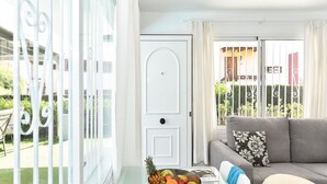 Un salon moderne avec un canapé gris, un saladier de fruits posé sur une table et une vue sur un jardin, visible à travers une porte vitrée.