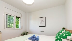 A bedroom with a bed, a window, a framed quote on the wall, and a small plant.