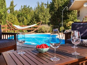 Ein Holztisch mit drei Weingläsern und einer Schale Kirschen neben einem Pool.