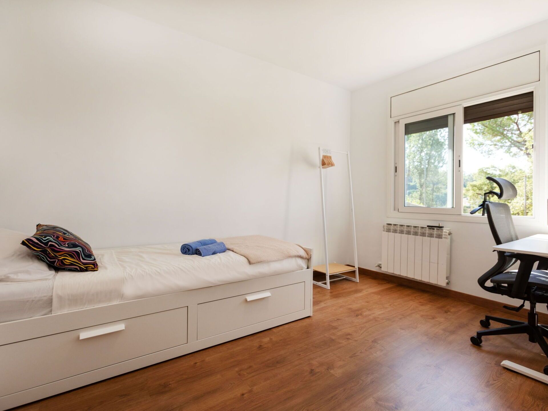 Une petite chambre à coucher au style minimaliste, avec un lit simple, un bureau et une chaise.