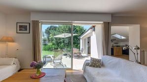 A spacious living area with a sofa, a wooden table with a vase, and a view of an outdoor patio with chairs and a table.