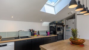 A modern kitchen with black cabinets, a wooden countertop, a skylight, and pendant lighting.