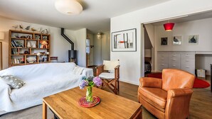 A modern bedroom with a large bed, a wooden side table with a vase of flowers, a leather armchair, and a bookshelf filled with books and decorative items.