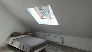 Un dormitorio con techo inclinado, una cama, una mesita de noche, un radiador y una ventana con cortinas.