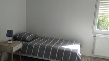 Un dormitorio pequeño con una cama individual, una mesita de noche, una lámpara y una ventana con persianas.