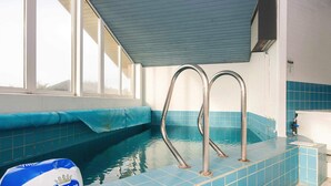 Ein Hallenbad mit blauen Fliesen, Metallleiter und einem blau-weißen Ball.