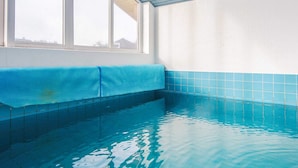 Ein Schwimmbecken mit klarem, blauem Wasser, einer blauen Matte am Rand und Blick zum Himmel durch ein Fenster.