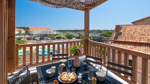 En balkon med et spisebord, der vender ud over et kystlandskab med bygninger og en klar himmel.