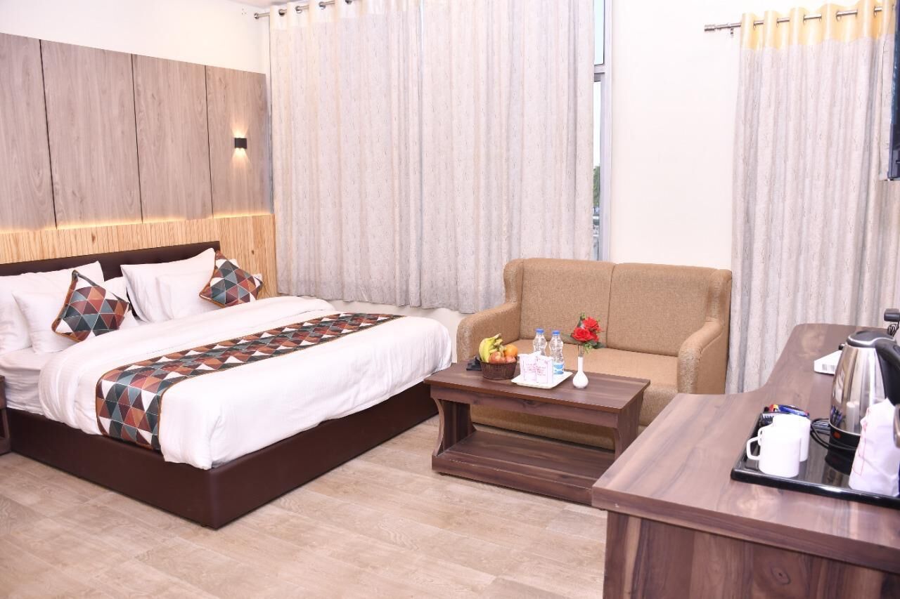 A hotel room with a bed, a sofa, a coffee table, and a desk with a kettle and mugs.