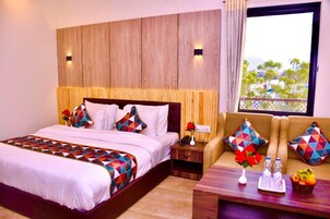 Habitación de hotel con una cama grande, un sofá, cabecera de madera y ventana con vistas.