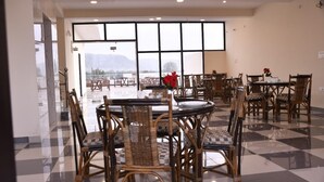 A dining area with wicker chairs and tables, large windows with a mountain view, and a checkered floor. - Hotel Saif Ranthambore (Sawai Madhopur)